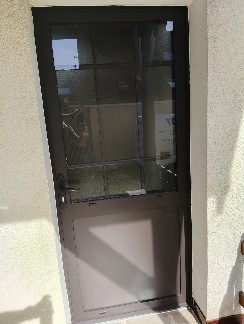 Pose d'une porte d'entrée en aluminium brun avec petits bois intégrés et vitrage brouillé.